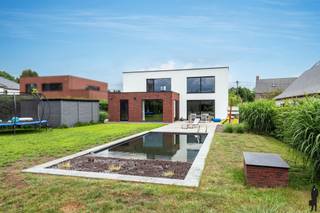 <p><strong>Ruime woning met multifunctionele studio</strong></p>
<p>In een <strong>rustige en aangename woonwijk</strong> te <strong>Vlimmeren</strong> bevindt zich deze verrassend ruime woning boordevol mogelijkheden voor <strong>grote gezinnen</strong>, <strong>thuiswerkers</strong> of wie op zoek is naar een combinatie van wonen, werken en ontspannen onder één dak.</p>
<p>De woning onderscheidt zich door haar <strong>royale leefruimtes</strong> en de aanwezigheid van een <strong>volledig aparte studio met eigen ingang</strong>. Deze multifunctionele ruimte biedt tal van mogelijkheden en kan perfect ingericht worden als <strong>zorgwoning</strong>, <strong>praktijkruimte voor een vrij beroep</strong>, <strong>kantoor</strong>, <strong>hobbyruimte</strong>, <strong>gastenverblijf</strong> of als woonunit voor een inwonend familielid. Dankzij de verbinding via de <strong>ruime garage</strong> blijven beide delen van de woning bovendien praktisch met elkaar verbonden.</p>
<p>Bij het betreden van de hoofdwoning komt u terecht in een <strong>ruime inkomhal</strong>, die toegang biedt tot de verschillende leefruimtes. De <strong>lichtrijke woonkamer</strong> vormt samen met de <strong>royale leefkeuken met kookeiland</strong> het hart van de woning. Aansluitend bevinden zich een bijkeuken en een <strong>speelkamer</strong>, die eveneens perfect kan dienen als bureau of hobbykamer.</p>
<p>Op de verdieping bevinden zich twee bijzonder ruime slaapkamers, waaronder een <strong>master bedroom</strong>, aangevuld met een <strong>grote dressing/inloopkast</strong>, een badkamer en een apart toilet. De extra leefruimte op deze verdieping biedt bovendien de mogelijkheid om, mits enkele beperkte aanpassingen, een <strong>volwaardige derde slaapkamer</strong> te creëren.</p>
<p>De studio beschikt over een eigen inkomhal, een aangename leefruimte met <strong>open keuken</strong>, een slaapkamer, bergruimte, een badkamer en een apart toilet. Hierdoor kan deze ruimte volledig zelfstandig functioneren en biedt ze maximale flexibiliteit voor diverse woon- of beroepsdoeleinden.</p>
<p>Ook buiten heeft deze woning heel wat te bieden. De <strong>volledig omheinde tuin</strong> garandeert optimale privacy en vormt een heerlijke plek om te ontspannen. Het <strong>zwembad</strong> zorgt voor een extra vleugje luxe en vakantiegevoel, terwijl de ruime, dubbele garage voldoende plaats biedt voor voertuigen, fietsen en extra opslagruimte.</p>
<p>Een eigendom dat dankzij haar <strong>ruimte</strong>, <strong>veelzijdigheid</strong> en <strong>uitstekende indeling</strong> perfect inspeelt op de woonnoden van vandaag en morgen. Een unieke opportuniteit voor wie op zoek is naar een woning met net dat beetje meer.</p>