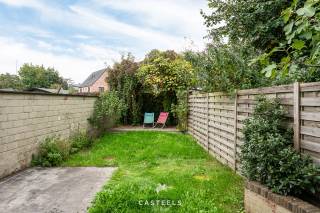 Deze rijwoning in de Loofblommestraat combineert een praktische indeling met een fijne buitenruimte. Met twee ruime slaapkamers, een zolder met mezzanine en een tuin met terras is ze geschikt voor wie comfortabel wil wonen, dicht bij alle voorzieningen.<br /><br />Leefruimte<br />De living is het hart van de woning. De parketvloer geeft de ruimte een warme uitstraling. De houtkachel zorgt in de koudere maanden voor gezelligheid en extra comfort.<br />Vanuit de leefruimte bereikt u het terras en de tuin. Zo loopt binnen en buiten vlot in elkaar over.<br /><br />Slaapkamers en zolder<br />Op de 1ste verdieping bevinden zich twee ruime slaapkamers.<br />Daarboven ligt nog een zolder met mezzanine en lavabo. Deze ruimte biedt mogelijkheden: een bureau om thuis te werken, een hobbyruimte of een extra plek voor logees. U kiest zelf wat het best bij uw manier van wonen past.<br /><br />Badkamer en wasruimte<br />De badkamer is voorzien van zowel een bad als een inloopdouche. Daarnaast is er een aparte wasruimte. Wasmachine en droogkast staan zo uit het zicht en de badkamer blijft een rustige ruimte.<br /><br />Tuin, terras en zij-ingang<br />Het terras en de tuin zijn een fijne plek om buiten te zitten of te ontspannen.<br />Een praktische troef is het poortje aan de zijkant van de woning. Fietsen en vuilnisbakken brengt u zo rechtstreeks naar achteren, zonder door de woning te moeten. Voor een rijwoning is dat een comfort dat u dagelijks merkt.<br /><br />Ligging<br />De woning ligt centraal, met de dagelijkse voorzieningen op korte afstand. Bakker, slager en frituur bereikt u te voet. Ook de Carrefour Hypermarkt ligt op wandelafstand.<br /><br />Voor gezinnen is de nabijheid van basisschool Westerhem, om de hoek, een duidelijk pluspunt.<br /><br />Ook de bereikbaarheid zit goed:<br />De bushalte Loofblommestraat ligt op minder dan 100 meter.<br />Een Blue-bike-station vindt u in het dorpscentrum.<br />Met de wagen zit u snel op de E40.<br />Het centrum van Gent is vlot bereikbaar.