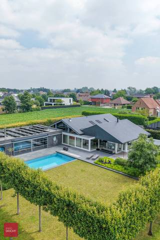 Afgeschermd van straatbeeld en met toegangsdreef bereikbaar. Ruime tijdloos hernieuwde villa (462m² vloeroppervlakte) bestaande uit een inkomhall, living met open haard, ingerichte keuken (Fraeye), eetruimte, annex berging met toegang tot mooie kelder en zolder, 3 slaapkamers (1 beneden), badkamer en bureel op verdieping. Aangesloten uitbouw met hoofdslaapkamer / dressing, / badkamer, leefruimte met open haard, sauna, ontspanningsruimte, technische ruimte. Garage voor 2 wagens, carport met tuinberging en parking. Zwembad (Bob Monteyne) met buitendouche. Alle modern comfort (vloerverwarming, 59m² zonnepanelen met groenestroomcertificaten tot 2032, 20.000 l regenwater etc)