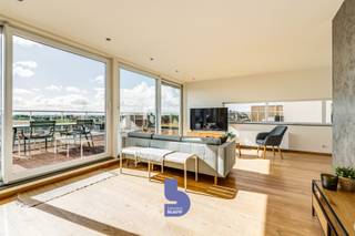 Ruimte, licht en een uitzonderlijk terras op een toplocatie. Dit prachtige duplex penthouse is gelegen op de 4de verdieping van de klassevolle residentie ‘Fusion’, een recente residentie uit 2008. Dankzij de centrale ligging bevinden winkels, openbaar vervoer, het strand en belangrijke invalswegen zich allemaal binnen handbereik.<br /><br />Met maar liefst 133 m² bewoonbare oppervlakte, drie slaapkamers en een riant, zonovergoten terras biedt dit penthouse een uitzonderlijk gevoel van ruimte en comfort.<br /><br />Bij het binnenkomen ervaar je meteen het WOW-effect. De bijzonder lichtrijke woonkamer baadt in het zonlicht en geniet rondom van terrassen, waardoor binnen en buiten hier perfect in elkaar overvloeien.<br /><br />De aangename parketvloer zorgt voor een warme en stijlvolle uitstraling. Er is voldoende ruimte voor een ruime zithoek en een aparte eetruimte, terwijl de grote keuken aansluit op de leefruimte en bovendien beschikt over een extra berging.<br /><br />De nachthal geeft toegang tot drie volwaardige slaapkamers, een badkamer met comfortabele inloopdouche en een apart toilet.<br /><br />Maar de absolute troef van dit penthouse is zonder twijfel het riante terras. Hier geniet je volop van de zon, de openheid en het mooie zicht rondom. Op heldere dagen reikt het zicht zelfs tot aan de zee in de verte. Een heerlijke plek om te ontbijten in de ochtendzon, lang te tafelen met vrienden of simpelweg te genieten van de rust en het uitzicht.<br /><br />De combinatie van de royale bewoonbare oppervlakte, de overvloedige lichtinval, de verschillende terrassen, drie slaapkamers en de uitstekende ligging maakt van dit duplex penthouse een bijzonder aangename woonst. Bovendien geniet je in deze recente residentie van een uitstekend EPC-label B en zijn er een gemeenschappelijke fietsenberging en afvalberging aanwezig.
