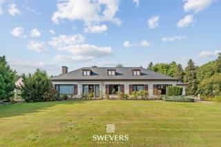 Voor meer info en foto’s, surf naar www.swevers.be – Aan de Helzoldstraat 92 in Houthalen-Helchteren wacht een ruime open bebouwing op een perceel van bijna 40 are. Met een bewoonbare oppervlakte van 412 m² en een kelder van 209 m² is deze woning ideaal voor grote gezinnen, zelfstandigen of wie op zoek is naar extra wooncomfort. De woning werd deels vernieuwd in 2017 (verwarmingsinstallatie, keuken, badkamer, vloeren) en recent in 2024 voorzien van nieuwe ramen en elektrische rolluiken. Op het gelijkvloers tref je een ruime inkomhal, aparte vestiaire, lichtrijke leefruimte van 50 m², een vernieuwde keuken, drie slaapkamers, een badkamer, een apart toilet, een bijkeuken en een bureauruimte. Op de eerste verdieping is een aparte woonunit met leefruimte, keuken, badkamer en grote slaapkamer, perfect voor kangoeroewonen of dubbele bewoning. De kelder met dubbele garage is volledig uitgerust en toegankelijk via 2 sectionale poorten – ideaal als werk- of opslagruimte. Buiten geniet je van een prachtig aangelegde tuin met sproei-installatie, ruime oprit, extra garage en veel privacy. De woning ligt op korte afstand van winkels, scholen, ontspanning en de E314. Voor meer informatie, bel 011 255 155. Bron bewoonbare oppervlakte: EPC – verslag.