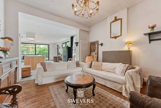 Voor meer info en foto’s, surf naar www.swevers.be – Op een centrale ligging in Maasmechelen vind je deze ruime halfopen bebouwing met een bewoonbare oppervlakte van 189 m² op een perceel van 688 m². De woning, gebouwd in 1933, biedt een degelijke basis en veel potentieel voor wie op zoek is naar een gezinswoning die nog naar eigen smaak opgefrist kan worden. Via de inkomhal bereik je de leefruimtes op het gelijkvloers. Vooraan bevinden zich twee aparte woonkamers die samen ongeveer 36 m² vormen en genieten van een aangename lichtinval. Achteraan werd een recente, ruime keukenuitbouw van circa 48 m² voorzien. Deze leefkeuken vormt het hart van de woning en biedt plaats voor een grote eettafel, extra kastruimte en een praktische inrichting. Vanuit de keuken is er een mooi zicht op de tuin en een vlotte toegang tot het terras. Verder is er op het gelijkvloers een apart toilet. Op de eerste verdieping bevinden zich momenteel twee volwaardige slaapkamers en een badkamer met douche en ligbad. De zolder is volledig ingericht en beschikt over twee slaapkamers. Daarnaast beschikt de woning over een kelder van ongeveer 30 m², ideaal als opslag-, hobby- of voorraadruimte. Het oostelijk georiënteerde perceel biedt heel wat buitenruimte en is ideaal voor gezinnen, tuinliefhebbers of wie graag buiten geniet. De ligging is praktisch: scholen, winkels, openbaar vervoer, restaurants en ontspanning bevinden zich in de nabije omgeving. Ook de autosnelweg, Terhills en Maasmechelen Village zijn vlot bereikbaar. Een woning met ruimte, karakter en veel mogelijkheden op een interessante locatie. Voor meer informatie, bel 011 255 155. Bron bewoonbare oppervlakte: EPC – verslag.
