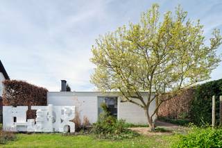 <em>Deze woning in Sint-Truiden is een uitzonderlijk voorbeeld van een kunstenaarswoning waarin architectuur, beeldende kunst en landschap in volledige symbiose samenkomen. Ontworpen in 1961 door architect Adolf Nivelle, in nauwe dialoog met de toenmalige bouwheer en kunstenaar Toon Vanmechelen, overstijgt deze woning het louter functionele wonen. Het is een plek waar denken, maken en leven samenkomen in één coherent geheel, gedragen door een sterke modernistische visie met uitgesproken brutalistische accenten.</em><br /><br /><strong>De signatuur van adolf nivelle</strong><br />Adolf Nivelle behoort tot een generatie architecten die zich bewust afzette tegen ornament en oppervlakkigheid, en resoluut koos voor een architectuur van essentie en structuur. Zijn werk wordt gekenmerkt door een helder constructief denken, een consequente materialiteit en een bijzondere gevoeligheid voor ruimte, licht en inplanting. In deze woning komt die visie tot volle maturiteit.<br />Nivelle benadert architectuur als een totaalkunstwerk waarin elk element — van dragende structuur tot detailafwerking — deel uitmaakt van een groter geheel. De strakke geometrie, de ritmiek van horizontale lijnen en de zorgvuldige positionering op het perceel tonen een architect die niet enkel bouwt, maar componeert. De woning is geen object op zich, maar een ruimtelijke ervaring die zich ontvouwt in relatie tot haar omgeving.<br /><br /><strong>De kunstenaar als medeschepper</strong><br />De aanwezigheid van kunstenaar Toon Vanmechelen als bouwheer en mededenker geeft deze woning een extra gelaagdheid. Dit is geen klassieke samenwerking waarbij kunst pas nadien wordt toegevoegd, maar een intrinsieke verweving van kunst en architectuur vanaf de eerste schets. De woning werd opgevat als een leef- en werkplek waarin artistieke expressie een vanzelfsprekende plaats krijgt.<br />De beeldhouwwerken en artistieke ingrepen, zowel in de tuin als in de overgangszones van de woning, functioneren niet als decoratie maar als ruimtelijke ankerpunten. Ze begeleiden de beweging doorheen het huis, creëren accenten en versterken de beleving van schaal en perspectief. De patio en voortuin worden zo verlengstukken van het atelier, terwijl het interieur een subtiele galerie wordt waarin kunst en dagelijks leven elkaar ontmoeten.<br /><br /><strong>Architectuur, kunst en tuin in dialoog</strong><br />Wat deze woning bijzonder maakt, is de continue dialoog tussen de rationele helderheid van de architectuur, de expressieve kracht van de kunst en de verstilde aanwezigheid van de tuin. Waar Nivelle structuur, rust en orde brengt, voegt Vanmechelen een meer intuïtieve, sculpturale laag toe. De tuin vormt daarin geen decor, maar een wezenlijk onderdeel van de woonbeleving.<br /><br />Met grote zorg werd het domein aangelegd en onderhouden, niet volgens een strak Frans schema, noch volgens een uitgesproken Engelse traditie, maar veeleer vanuit het gevoel en de intuïtie van de eigenaar. Die persoonlijke benadering geeft de buitenruimte een bijzondere zachtheid en vanzelfsprekendheid. De bloei begint vroeg in het seizoen met de magnolia, waarna de tuin zich verder ontvouwt in een bijna continue opeenvolging van kleuren, texturen en geuren. Doorheen het jaar blijft zij in beweging, levendig en toch sereen.<br /><br />Eens op het domein komt men in een oase van rust terecht, waarin de tuin een hoofdrol speelt. Grote glaspartijen kaderen zichten op het groen en op de aanwezige sculpturen, waardoor binnen en buiten, kunst en natuur, voortdurend met elkaar verweven blijven. De tuin verzacht de kracht van de architectuur, zonder haar te verzwakken, en versterkt tegelijk het contemplatieve karakter van de woning.<br /><br /><strong>Een leefomgeving voor makers</strong><br />De indeling en ruimtelijke opbouw van de woning verraden haar oorsprong als kunstenaarswoning. Naast de genereuze leefruimtes en slaapkamers is er expliciet ruimte voorzien voor creatie, reflectie en experiment. De aanwezigheid van een atelier en de flexibele invulling van verschillende ruimtes maken het geheel bijzonder geschikt voor wie wonen en werken wil combineren.<br />Tegelijk blijft de woning in haar opzet bijzonder helder en functioneel. De circulatie is logisch, de ruimtes zijn goed geproportioneerd en het daglicht wordt op een doordachte manier doorheen het huis geleid. Dit zorgt voor een leefkwaliteit die, ondanks de uitgesproken architecturale identiteit, bijzonder comfortabel en vanzelfsprekend aanvoelt.<br /><br /><strong>Een erfstuk met toekomst</strong><br />Hoewel de woning vandaag een energetische update vraagt, blijft de architecturale basis uitzonderlijk waardevol. De robuuste structuur en de sterke ontwerpvisie bieden een solide kader voor een hedendaagse interpretatie, waarbij duurzaamheid en comfort kunnen worden geïntegreerd zonder het karakter aan te tasten.<br /><br />Deze woning is meer dan een plek om te wonen. Het is een erfstuk waarin architectuur, kunst en landschap elkaar versterken — een omgeving die inspireert, vertraagt en verdiept. Een zeldzame kans voor wie op zoek is naar een woning met een verhaal, een ziel en een uitgesproken identiteit.<br /><br /><strong>Meer ontdekken?</strong><br />Wil je graag thuiskomen in deze uitzonderlijke woning?<br />Contacteer mij dan snel voor meer info of een persoonlijk bezoek ter plaatse!<br /><br /><em>De vermelde oppervlaktes zijn slechts indicatief. Katrien Wouters - creating IMMOtions kan niet verantwoordelijk gesteld worden voor de juistheid van de aan haar verstrekte gegevens.  </em>