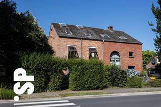 <strong>Crepain’s signatuur: een introverte blik op het moderne wonen<br /></strong>Vanaf zijn eerste realisaties hanteerde Crepain een uitgesproken persoonlijke vormentaal. De woning getuigt daarvan: een bakstenen gevel met karakteristieke vooruitgeschoven 'zichtvensters', die tegelijk sculpturaal en functioneel zijn. Achter deze eerder gesloten gevel ontvouwt zich een verrassend interieur, opgebouwd uit split-levels en loopbruggen die de binnenruimte doen aanvoelen als een gelaagd landschap. De woning benut zenitaal licht om zelfs de diepste zones tot leven te brengen — een subtiel spel van licht en schaduw, van geborgenheid en openheid.
<p><br /><strong>Een omgeving die rust en kwaliteit uitstraalt<br /></strong>De ligging van deze woning onderstreept haar stille karakter. Daarbovenop vormt Kalmthout als gemeente een van de aantrekkelijkste woonomgevingen in de regio. Niet toevallig werd Kalmthout recent uitgeroepen tot de gelukkigste gemeente van Vlaanderen<strong>. </strong>De nabijheid van het uitgestrekte natuurreservaat de Kalmthoutse Heide – op wandel- of fietsafstand – maakt deze plek bijzonder geliefd bij mensen die bewust kiezen voor een evenwicht tussen rust, natuur en bereikbaarheid. Het dorp kent een lange traditie als buitenverblijf voor Antwerpse stedelingen, net vanwege zijn unieke ligging en groene karakter. Vandaag vormt het een duurzame woonkeuze voor wie levenskwaliteit centraal stelt.</p>
<span><br /><strong>Parkzicht en privacy in balans<br /></strong>De woning geniet een bijzonder rustige ligging tegenover een publiek groenpark, wat zorgt voor een visuele ademruimte en een open uitzicht. Tegelijk garandeert het introverte karakter van het ontwerp maximale privacy — een unieke combinatie van beschutting en natuurlijke sereniteit. Achteraan sluit een wonderlijk organisch aangelegde tuin aan op de architectuur, met een speels ritme van groenstructuren en wandelpaden — een stille extensie van de woning, ontworpen om in elk seizoen te verrassen.<br /><br /><strong>Materialiteit en maatwerk<br /></strong>De gekozen materialen weerspiegelen de experimentele sfeer van de jaren ’70: zichtbeton, grenenhouten schrijnwerk, en vaste interieurelementen op maat ontworpen. Elk onderdeel — van deur tot vensterbank — draagt het stempel van een doordachte ontwerpfilosofie waarbij structuur en inrichting naadloos samenkomen.<br /><br /><strong>Over Jo Crepain (1950–2008)<br /></strong>Geboren in Brugge, opgeleid aan het Henri Van de Velde Instituut, groeide Jo Crepain uit tot een van de meest invloedrijke Belgische architecten van zijn generatie. Zijn carrière kende een vliegende start met de bekroonde woning Roels in Kapellen, nog ontworpen als student. Nadien volgden meer dan 750 projecten in binnen- en buitenland, variërend van particuliere woningen tot stedelijke herontwikkelingen. Hij was medeoprichter van het ontwerpbureau SILO en doceerde decennialang aan architectuuropleidingen in Gent, Rotterdam en Antwerpen. Zijn latere werk werd gekenmerkt door een postmoderne beeldtaal, met iconische projecten zoals de villa De Wachter in ’s Gravenwezel en het UCO-kantoor in Gent. Jo Crepain overleed in 2008, maar zijn nalatenschap leeft voort via Crepain Binst Architecture — het bureau dat hij samen met Luc Binst oprichtte.<br /><br /><strong>Een huis als ruimtelijke beleving<br /></strong>De woning aan de Voetbooglaan is een zeldzaam goed bewaard voorbeeld van Crepain’s vroege, conceptuele architectuur. Ze nodigt uit tot traag wonen, tot het ontdekken van vergezichten binnenin, en het ervaren van intimiteit zonder geslotenheid. Deze woning belichaamt de geest van een periode waarin architectuur opnieuw werd uitgevonden — helder, ruimtelijk en afgestemd op een bewuste manier van leven.<br /></span>