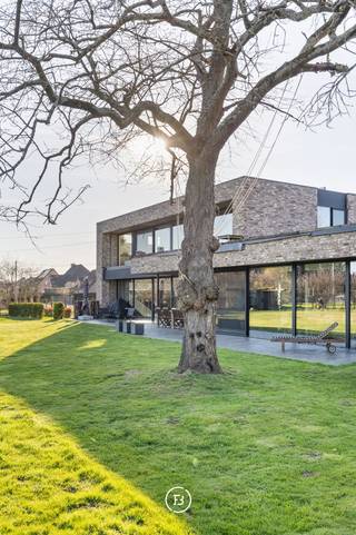 Deze moderne villa uit 2016 is gelegen op een uitzonderlijk breed perceel van ruim een halve hectare (5.016 m²) en combineert hedendaags comfort met een rustige, groene omgeving. Het ontwerp kenmerkt zich door een tijdloze architectuur, waarbij de indrukwekkende raampartijen zorgen voor een uitzonderlijke lichtinval en een naadloze overgang tussen binnen en buiten.<br /><br />De woning is ook praktisch ingericht voor wie wonen en werken wil combineren. Er zijn twee ruimtes voorzien die geschikt zijn voor een professionele activiteit aan huis. <br /><br />In de leefruimte staat ruimtelijkheid en wooncomfort centraal.<br /><br />De keuken is volledig uitgerust met premium toestellen van Gaggenau en een Quooker-kraan. Van hieruit, alsook de gehele leefruimte, geniet u van een weids vergezicht over de zuidoost georiënteerde tuin en de achterliggende natuur. <br /><br />Achter de keuken bevindt zich praktisch een grote berging, die ook toegankelijk is via de carport. Over de gehele woning zijn voldoende maatkasten voorzien, een tweede grote berging en een aparte wasruimte die ook van een douche is voorzien.<br /><br />De woonbeleving wordt verder naar een hoger niveau getild door een slim domoticasysteem, camerabewaking, alarmsysteem en een geïntegreerde muziekinstallatie die doorheen de woning voor de juiste sfeer zorgen.<br /><br />In totaal zijn er vijf slaapkamers en twee badkamers. De master bedroom beschikt over een ensuite badkamer en dressing met zicht op het groen, wat zorgt voor een rustige en aangename sfeer.<br /><br />Met een energielabel A en conforme elektriciteit is ook aan duurzaamheid en technische kwaliteit gedacht, wat het geheel toekomstgericht maakt. Deze lichtrijke villa vormt zo een perfecte balans tussen moderne architectuur, comfort en een unieke ligging in het groen.