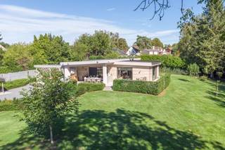 Century21 ImmoNero presenteert deze prachtig gerenoveerde bungalow woning van 221m² met uitzonderlijke afwerking, in een schitterende parktuin van 3.771m² welke u absolute rust en privacy waarborgt Via de electrische toeganspoort komt u het domein binnen langs de brede, verlichte privéoprit met een 6 tal parkeerplaatsen. De bungalow welke zeer grondig en volledig werd vernieuwd in 2020 -2025 biedt vervolgens: Inkom met WC, schitterende living met hypergeinstalleerde keuken van 78m², welke naadloos doorloopt in de prachtig aangelegde terrassen met subliem zicht op de parktuin; Ingerichte wasplaats 7m² en 2 kinderkamers van elk 12m² met ingemaakte kasten, Douchekamer; Masterbedroom bestaande uit Ingerichte dressing, kamer 26m² en en suite badkamer. Grote garage van 21m², Carport voor 2 wagens en tuinberging. Verwarming met Warmtepomp, zonnepanelen en Airco in alle ruimtes. Alu ramen, ventilatie D, Laadpaal, Camerabewaking rondom, Electriciteit is conform. EPC = B