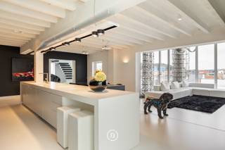 Au cœur de Diest se trouve ce loft d’exception, conçu par PCp Architects. Son architecture se distingue par une esthétique minimaliste en noir et blanc, des lignes épurées et un travail sur mesure soigné. Les rangements intégrés et les techniques dissimulées renforcent le caractère épuré de l’intérieur. Le loft offre 285 m² de surface habitable, complétés par une terrasse sur le toit d’environ 100 m² et une vue panoramique sur la ville.<br /><br />L’espace de vie constitue le cœur du loft et associe de généreuses proportions, de grandes baies vitrées et une cheminée ouverte. La cuisine entièrement équipée comprend notamment un wok intégré. Les appareils électroménagers peuvent être dissimulés derrière un volet à commande électrique, préservant ainsi une esthétique parfaitement épurée.<br /><br />Le même niveau comprend deux chambres, chacune avec sa propre salle de bains, ainsi que de nombreux rangements intégrés.<br /><br />L’étage supérieur est dédié à la vie extérieure. De grandes baies coulissantes relient directement l’intérieur à la terrasse sur le toit. Un bar en fait un espace idéal pour recevoir, tandis qu’une pièce séparée peut être aménagée en bureau ou espace polyvalent.<br /><br />Le loft dispose également d’un garage pour deux voitures, un atout rare en plein centre-ville.