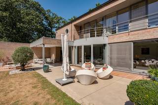 In de bijzonder gegeerde wijk <strong>Vriesdonk</strong> bevindt zich deze stijlvolle en uitstekend onderhouden villa op een royaal perceel van ca. <strong>2.043 m²</strong>. <br />De woning combineert een eigentijdse, luxueuze woonbeleving met een bijzonder veelzijdige indeling en biedt bovendien de mogelijkheid om <strong>wonen en professioneel werken</strong> op een discrete en comfortabele manier te verenigen.<br /> <br />De villa werd oorspronkelijk gebouwd in 1994 en in 2014 grondig gerenoveerd, waarbij gekozen werd voor een hoogwaardige afwerking, duurzame materialen en hedendaags wooncomfort.<br /> <br /><strong><u>Gelijkvloerse verdieping</u></strong><br />Via de verzorgde inkomhal met ingemaakte vestiaire betreedt u de woning. De ruime en bijzonder lichtrijke woonkamer van ca. <strong>40 m²</strong> is afgewerkt met parket en beschikt over een sfeervolle gashaard. Grote raampartijen zorgen voor een optimale lichtinval en creëren een mooie visuele en praktische verbinding met de tuin.<br />Aansluitend bevindt zich de stijlvolle eetkamer van ca. <strong>26 m²</strong>, eveneens voorzien van parket en uitgerust met een groot schuifraam dat rechtstreeks toegang biedt tot het terras.<br />De afzonderlijke designkeuken van ca. <strong>18 m²</strong> vormt een aangename leefruimte dankzij het ruime kook- en eeteiland. De keuken is volledig uitgerust met hoogwaardige <strong>Miele-inbouwtoestellen</strong>, waaronder een inductiekookplaat, vaatwasser, friteuse/grill, stoomoven, heteluchtoven en warmhoudplaat.<br /> <br />Aan de voorzijde bevindt zich een afzonderlijke bureau-/werkruimte van ca. <strong>9 m²</strong>, afgewerkt met parket en ingemaakte kasten. De plafondhoge ramen tot op de vloer zorgen hier voor een bijzonder aangename hoeveelheid natuurlijk daglicht.<br />Verder beschikt de woning over een uitzonderlijk ruime <strong>dubbele inpandige garage van ca. 60 m²</strong>, voorzien van een spoelbak. Vanuit de garage is er rechtstreeks toegang tot de tuin en een doorgang naar de wijnkelder van ca. <strong>7 m²</strong>.<br /> <br /><strong><u>Afzonderlijke praktijkruimte – ideaal voor zelfstandigen of vrije beroepen</u></strong><br />Een belangrijke troef van deze villa is de volledig uitgeruste praktijkruimte met een <strong>eigen ingang</strong>, waardoor professionele activiteiten perfect gescheiden kunnen worden van het privéleven.<br />De ruimte omvat een wachtzaal van ca. <strong>8 m²</strong>, voorzien van toilet en handenwasser, een berging en twee afzonderlijke bureauruimtes van ca. <strong>15 m² en 22 m²</strong>.<br />Dankzij de indeling en de afzonderlijke toegang biedt deze ruimte bovendien tal van alternatieve mogelijkheden. Zo kan ze, mits de nodige aanpassingen, worden ingericht als extra leefruimte, gastenverblijf, au-pairaccommodatie of als een volwaardige slaapkamer met badkamer op de begane grond. Ook voor <strong>kangoeroe wonen</strong> biedt de woning interessante mogelijkheden.<br /> <br /><strong><u>Eerste verdieping</u></strong><br />De nachthal, afgewerkt met parket en voorzien van ingemaakte kasten, leidt naar de verschillende slaapvertrekken.<br />Er zijn twee slaapkamers van ca. <strong>14 m² en 18 m²</strong>. Eén kamer beschikt over ingemaakte kasten, terwijl de andere toegang biedt tot een balkon met een prachtig uitzicht over de tuin.<br />De eerste badkamer is uitgerust met een ligbad, toilet en lavabo.<br />De royale hoofdslaapkamer van ca. <strong>20 m²</strong> vormt een aangename privésuite en beschikt over een ingemaakte dressing- en tv-kast. Vanuit de slaapkamer is er toegang tot een uitzonderlijk ruim terras van ca. <strong>22 m²</strong>, vanwaar een trap rechtstreeks naar de tuin leidt.<br />De aansluitende ensuite badkamer van ca. <strong>19 m²</strong> is ingericht met een dubbele lavabo, ruime inloopdouche en ligbad. Een afzonderlijk toilet vervolledigt deze verdieping.<br /> <br /><strong><u>Buitenruimte</u></strong><br />Rondom de villa bevindt zich een <strong>prachtig aangelegde en volledig omheinde tuin</strong>, aangelegd in 2014. Dankzij de ideale zonoriëntatie en de natuurlijke privacy vormt deze buitenruimte een bijzonder aangename verlenging van de woning.<br />Verschillende terrassen bieden de mogelijkheid om op elk moment van de dag van de tuin te genieten, waaronder een aangenaam <strong>overdekt terras</strong>.<br />Daarnaast zijn er een overdekte berging en twee tuinhuizen aanwezig.<br /> <br /><strong><em>Een stijlvolle, ruime en uitstekend onderhouden villa met een hoogwaardige afwerking die wonen, werken, privacy en comfort op een bijzonder geslaagde manier samenbrengt in het geliefde Vriesdonk.</em></strong><br /><strong><em> </em></strong><br />📞 Interesse? Contacteer ons voor meer informatie of een bezoek ter plaatse via jeffrey@jurimmo.be of via +32 474 04 13 26