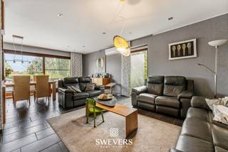 Voor meer info en foto’s, surf naar www.swevers.be – Ontdek deze uitzonderlijk ruime kangoeroewoning op een perceel van 19a 67ca in het gegeerde Kuringerheide, vlak bij Hasselt en natuurgebied De Platwijers. De woning werd gebouwd in 1980 en in 2006 functioneel omgevormd tot een volwaardige kangoeroewoning. Met een bewoonbare oppervlakte van 337 m², een gunstig EPC-label B en een praktische indeling is dit de ideale thuis voor grote gezinnen, inwonende familie of wie wonen en zorg wil combineren. De hoofdwoning beschikt over een lichtrijke leefruimte, keuken, bureau, slaapkamer en badkamer op het gelijkvloers. Op de verdieping bevinden zich meerdere slaapkamers, waardoor de woning in totaal zeven slaapkamers telt. Daarnaast zijn er drie badkamers aanwezig. De aparte woonunit beschikt over een eigen inkomhal, leefruimte met keuken, slaapkamer en badkamer, zodat privacy en zelfstandigheid verzekerd zijn. Onder de volledige woning bevindt zich een ruime kelder van 88 m², ideaal als opslag-, hobby- of werkruimte. Buiten geniet u van een dubbele carport, een zuidgerichte tuin en een heerlijk zwembad waar u in alle rust kan ontspannen. Airconditioning en rookdetectoren zorgen voor extra comfort. De woning biedt bovendien alle mogelijkheden om ze verder naar eigen smaak te moderniseren. Dankzij de rustige ligging bevinden scholen, winkels, openbaar vervoer en het centrum van Hasselt zich op korte afstand, terwijl ook de autosnelwegen vlot bereikbaar zijn. Een unieke eigendom met veel ruimte, flexibiliteit en toekomstmogelijkheden. Voor meer informatie, bel 011 255 155. Bron bewoonbare oppervlakte: EPC – verslag.