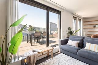 Deze instapklare penthouse is gelegen in de Lange Sint-Annastraat, een karaktervolle straat in het hart van Antwerpen, op het kruispunt van het Eilandje, de universiteitswijk en het historische centrum. Stijlvolle winkels, kwalitatieve horeca en culturele hotspots bevinden zich op wandelafstand, net als de Meir, Groenplaats en Grote Markt. Dankzij deze centrale ligging geniet u van het bruisende stadsleven, terwijl u bovenaan het gebouw in alle rust thuiskomt. Zowel openbaar vervoer als belangrijke invalswegen zijn vlot bereikbaar.<br /><br />Het appartement bevindt zich op de bovenste verdieping van een recente en verzorgde residentie. De lichtrijke leefruimte vormt het hart van het appartement en geeft via grote raampartijen toegang tot twee ruime zonneterrassen aan weerszijden. Dit zorgt de hele dag door voor overvloedig natuurlijk licht en een aangenaam panoramisch uitzicht over de stad. Aansluitend aan de leefruimte bevindt zich een aparte bureauruimte, ideaal als thuiswerkplek of in te richten als derde slaapkamer.<br /><br />De keuken is volledig uitgerust met kwalitatieve toestellen en een ruim werkblad, perfect voor wie graag kookt en gasten ontvangt. Verder beschikt het appartement over twee ruime slaapkamers, een modern afgewerkte badkamer met ligbad, inloopdouche en dubbel lavabomeubel, een apart gastentoilet en een praktische (was) berging. <br />Een privatieve kelderberging en gemeenschappelijke fietsenberging zijn inbegrepen. De aankoop van een ondergrondse autostaanplaats is mogelijk.